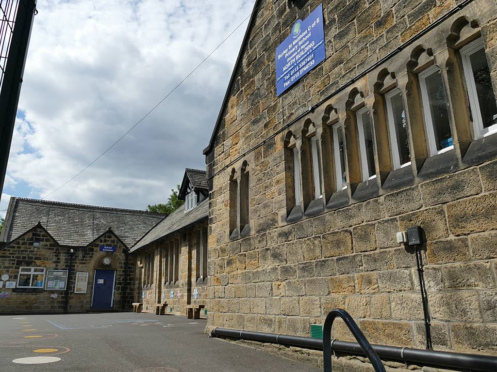 The stone north building of a primary school beside an empty playground, with the school entrance in the background
