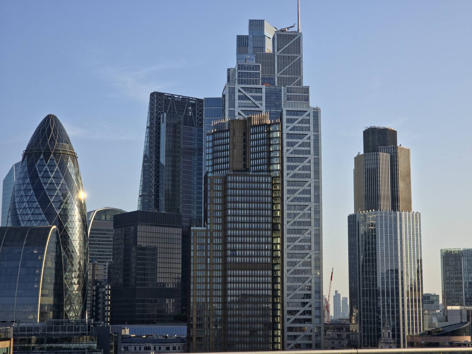 The towers of the City of London, including the Gherkin, in evening light against a clear sky