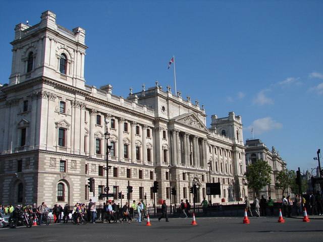 The full stone facade of the Treasury buildings in Whitehall with a crowd and traffic cones on the street in front