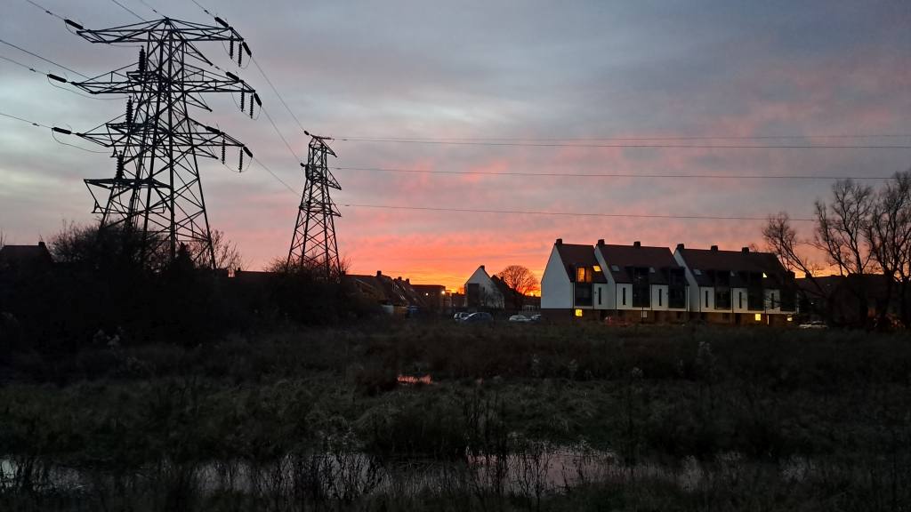Electricity pylons and power lines beside new homes at sunset, with lights on in the houses