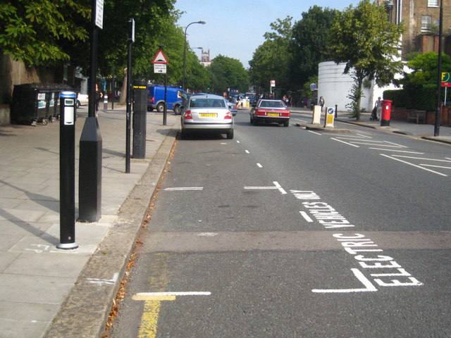 A London street with a black on-street charging post on the pavement and the words electric vehicles painted in a parking bay