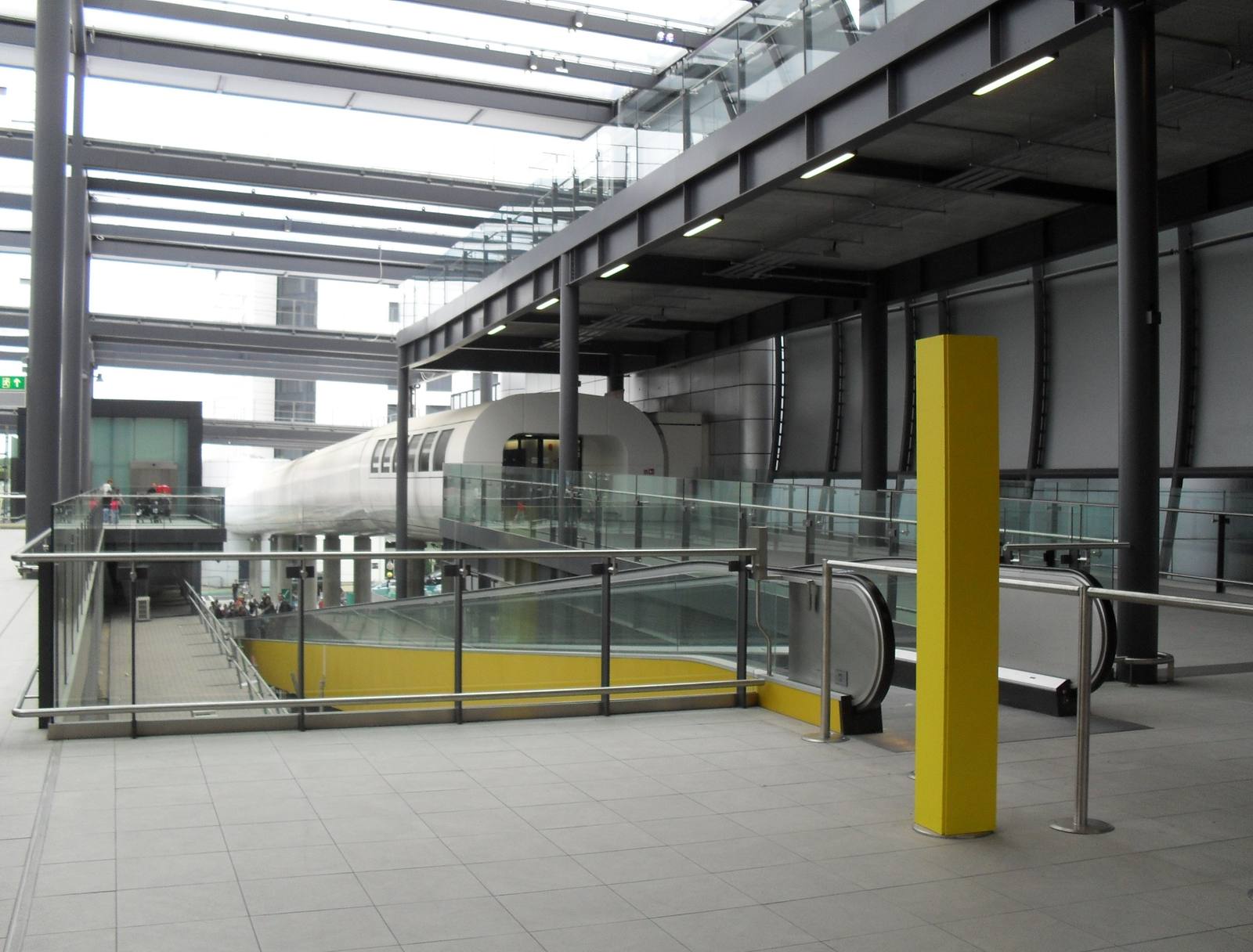 The interior of Gatwick Airport's North Terminal, with an escalator, glass balustrades and the inter terminal shuttle in the background