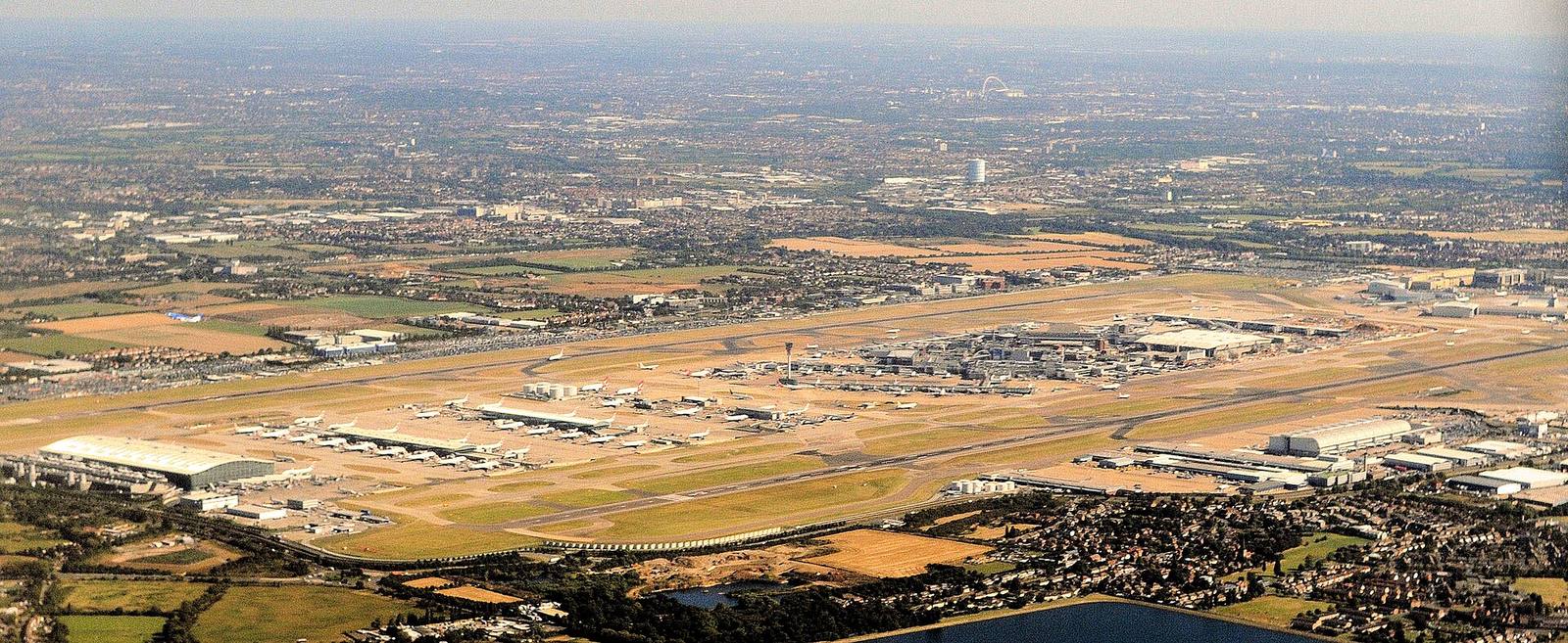 An aerial view of Heathrow Airport, with its two east to west runways, terminals and parked aircraft, and housing in the foreground