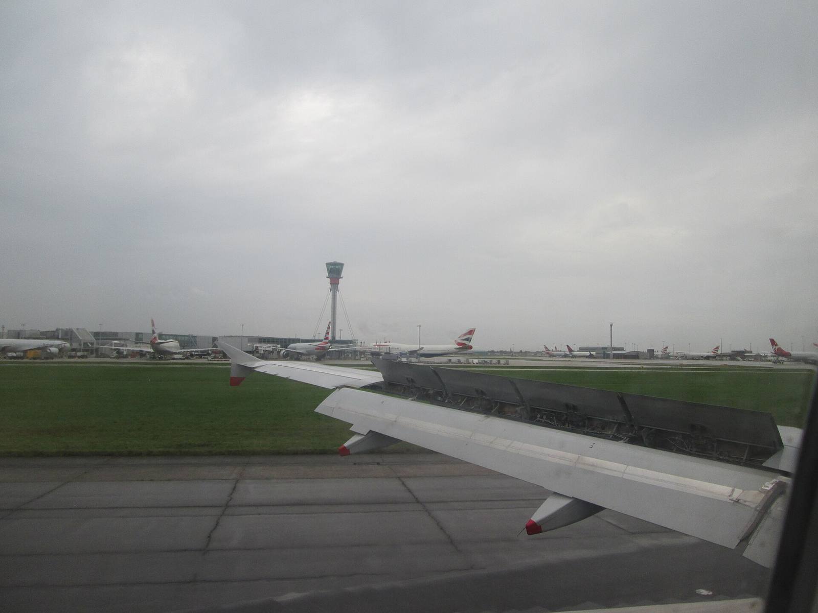 The wing of an aircraft after landing at Heathrow, with parked aircraft and the control tower across the airfield