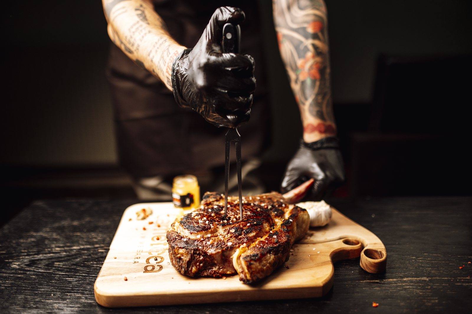 A chef's gloved hands carving a grilled steak on a wooden board in a kitchen