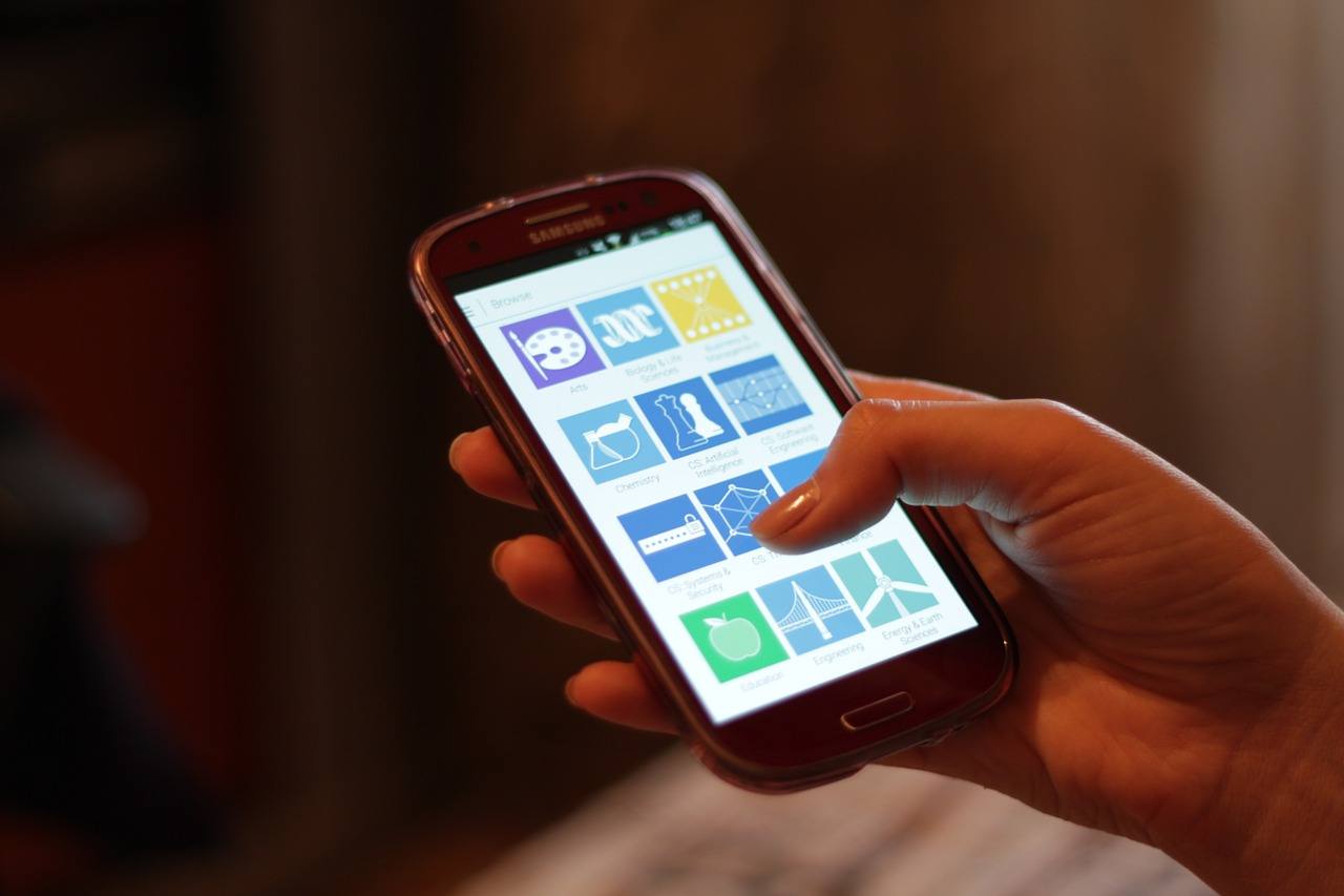 A hand holding a smartphone with a grid of app tiles on the screen