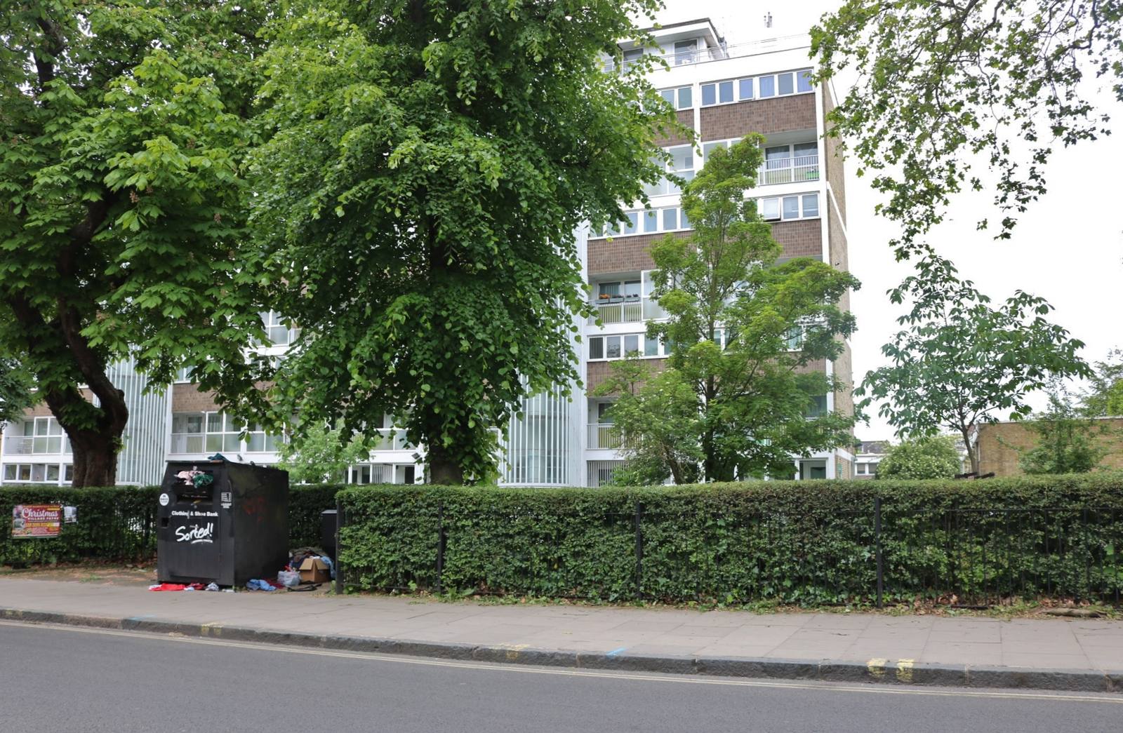 A tall council flat block seen behind trees and a hedge from Highgate Road in Gospel Oak, London
