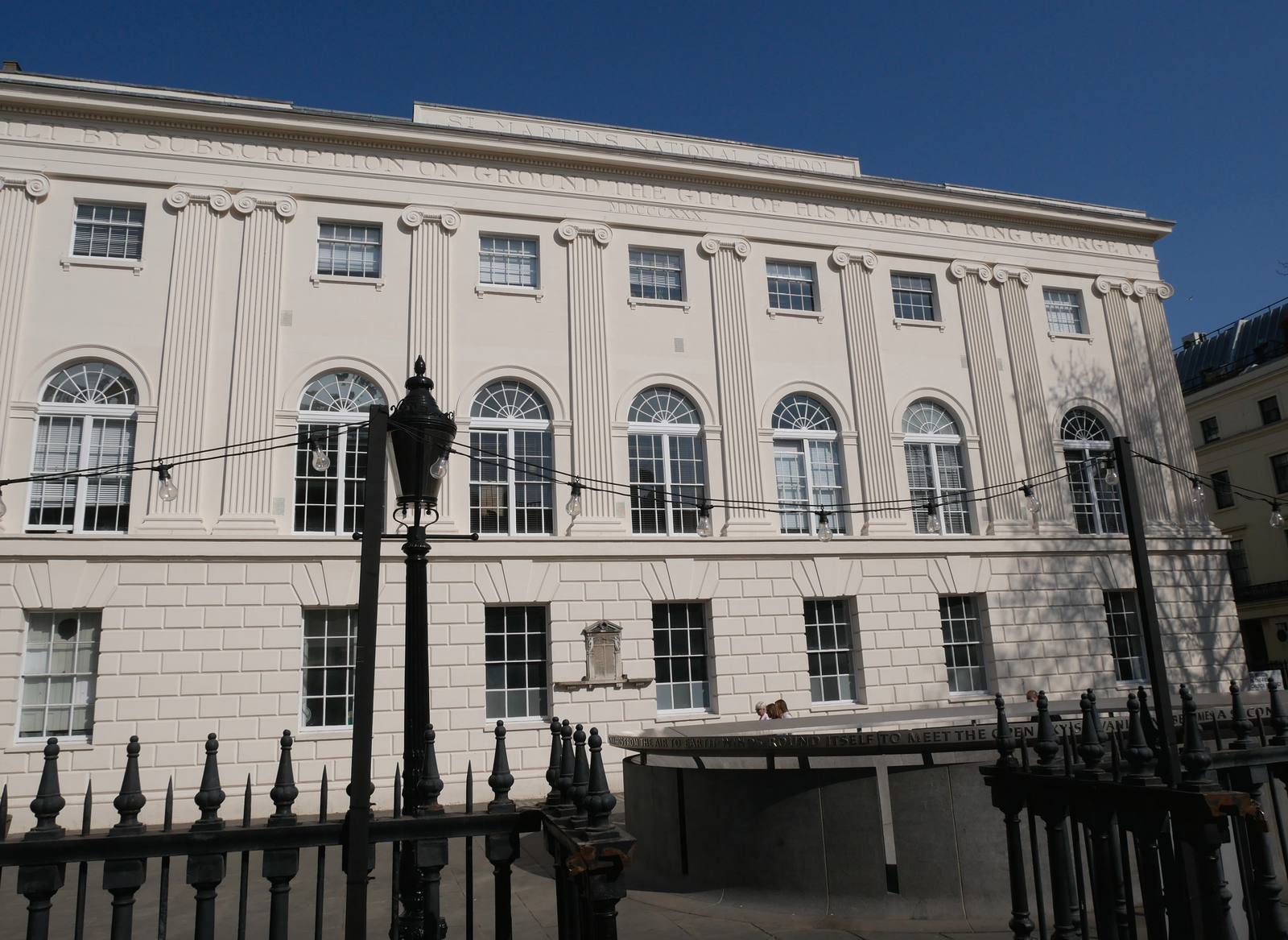 The white classical facade of the St Martin's school building in London, with arched windows, seen behind black railings