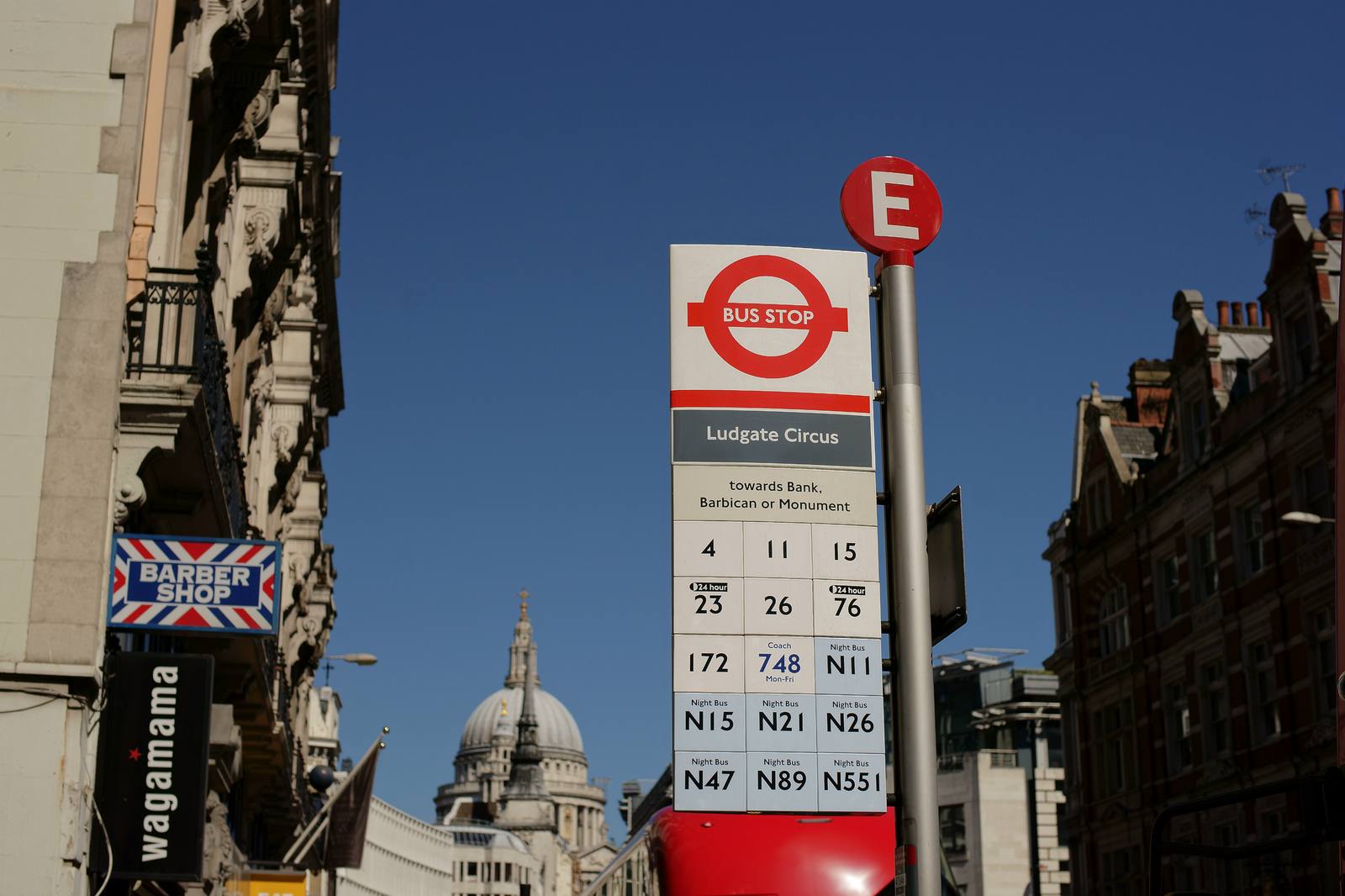 A London bus stop flag for Ludgate Circus against a blue sky, with the dome of St Paul's Cathedral in the background